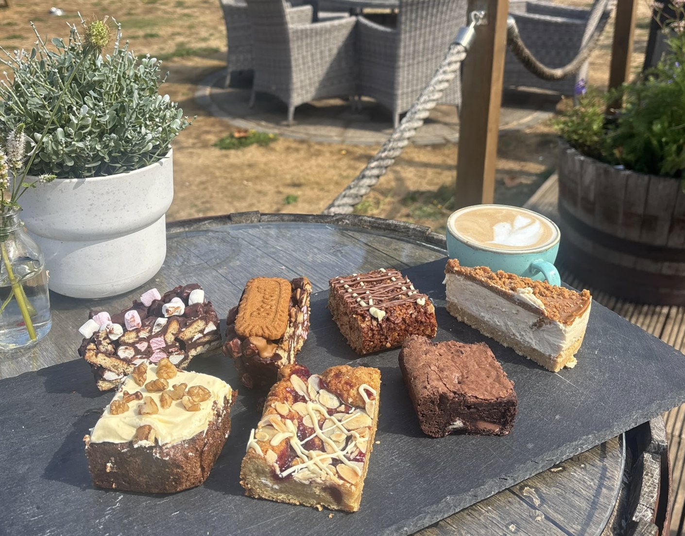 A slate board of homemade cakes and bakes with a latte in the garden